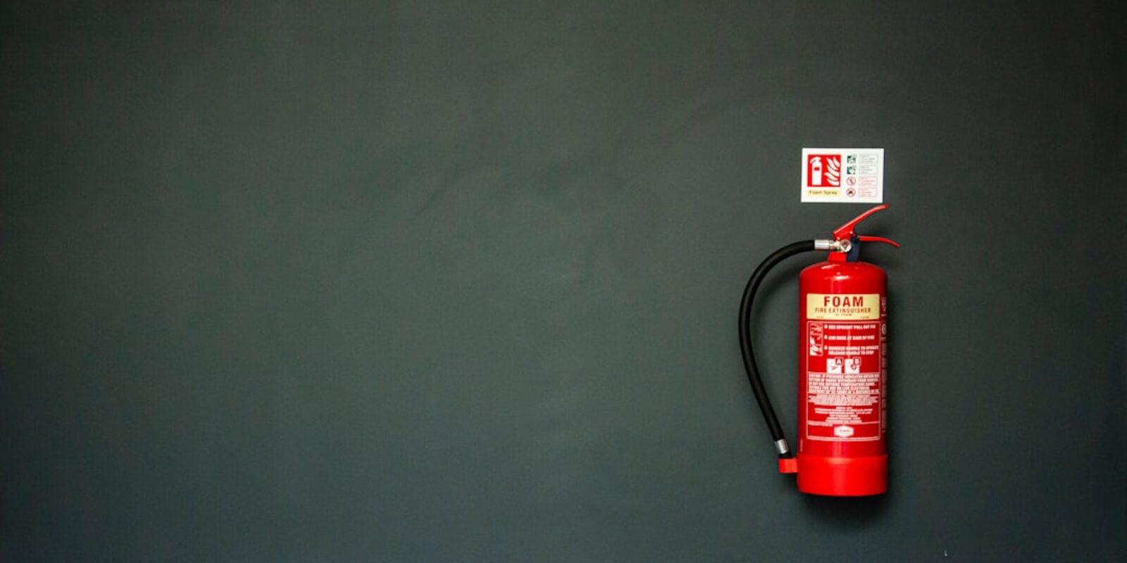 Red foam fire extinguisher mounted on a large dark wall beside its instruction placard